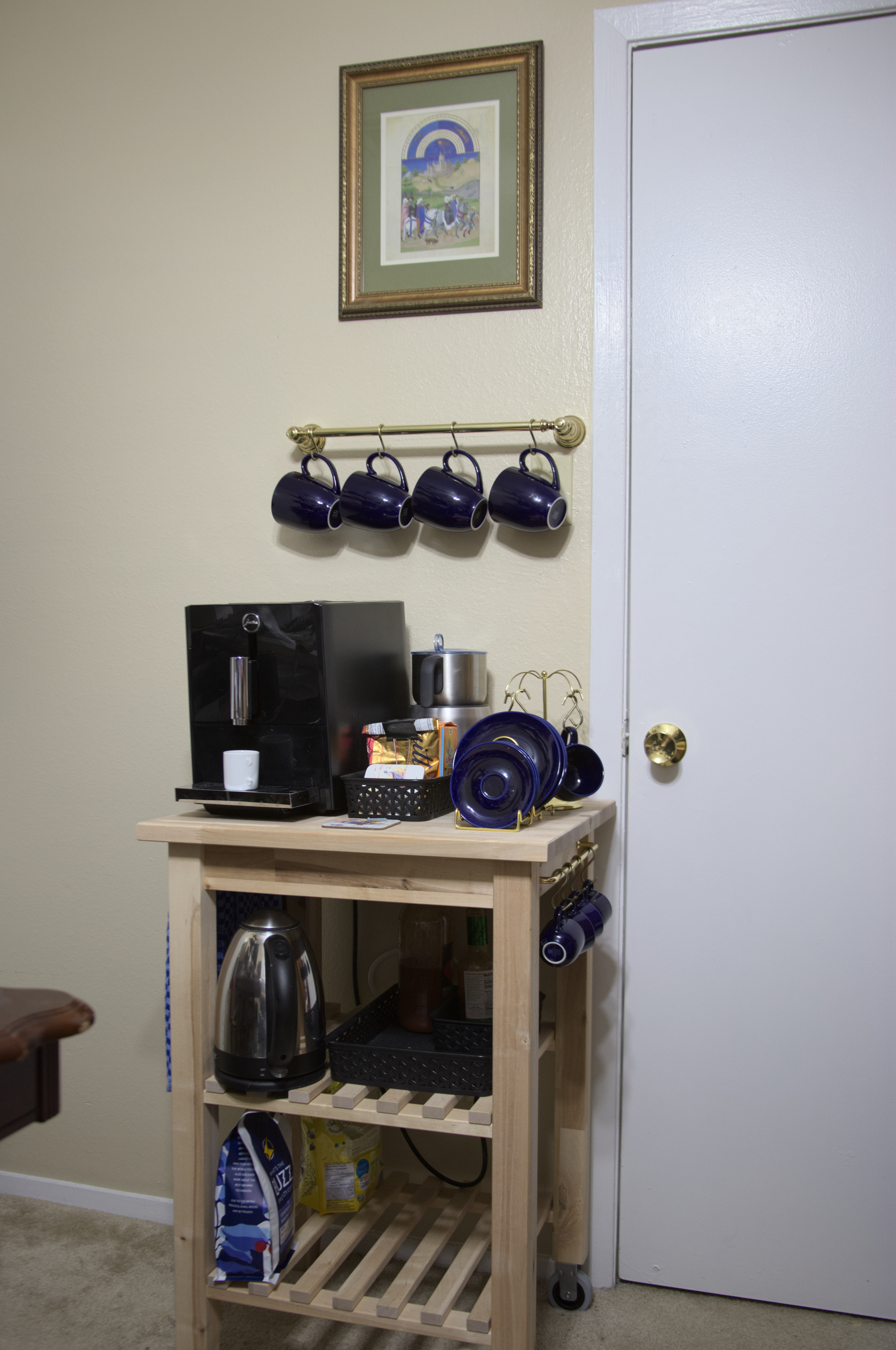 A picture of a coffeemaker, mugs, and a kettle on a kitchen island