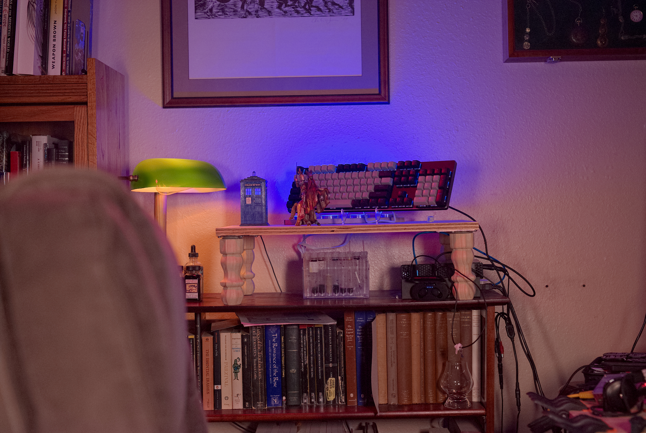 A picture of a chair turned to the side so you can see various items on top of a bookcase, such as a keyboard, a lamp, some ink bottles, and a couple of hard drives.