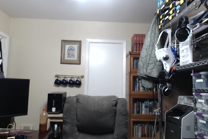 A picture of a closet with a coffee station to its left and a bookshelf to its right. A chair is in front of it.